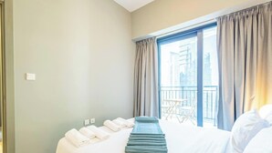 Et hotelværelse med en seng, et lille bord og udsigt til bygninger gennem vinduet.