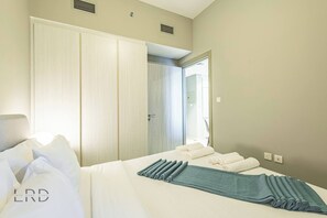Ein Hotelzimmer mit Bett, Kissen, einem gefalteten Handtuch, einem Kleiderschrank und einer Tür zu einem weiteren Raum.