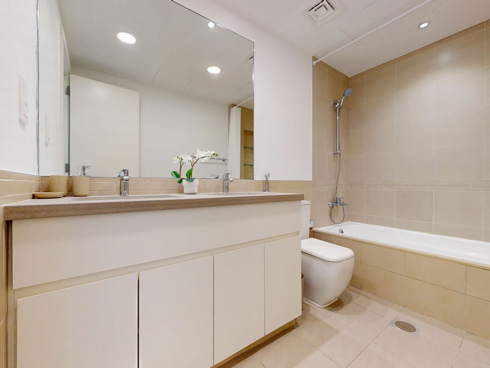 Une salle de bain moderne avec un grand miroir, un lavabo à deux cuves, des toilettes et une baignoire.