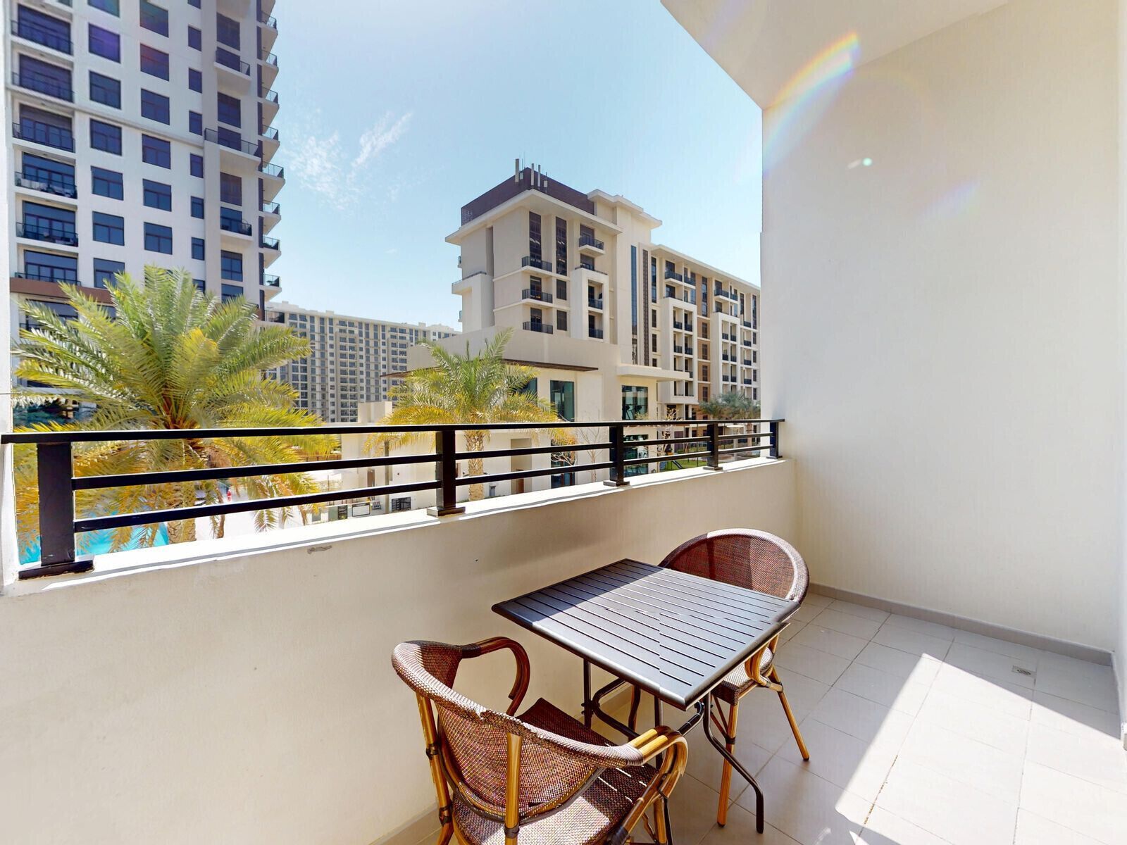 A balcony with a table and chairs, overlooking a residential area with buildings and palm trees.