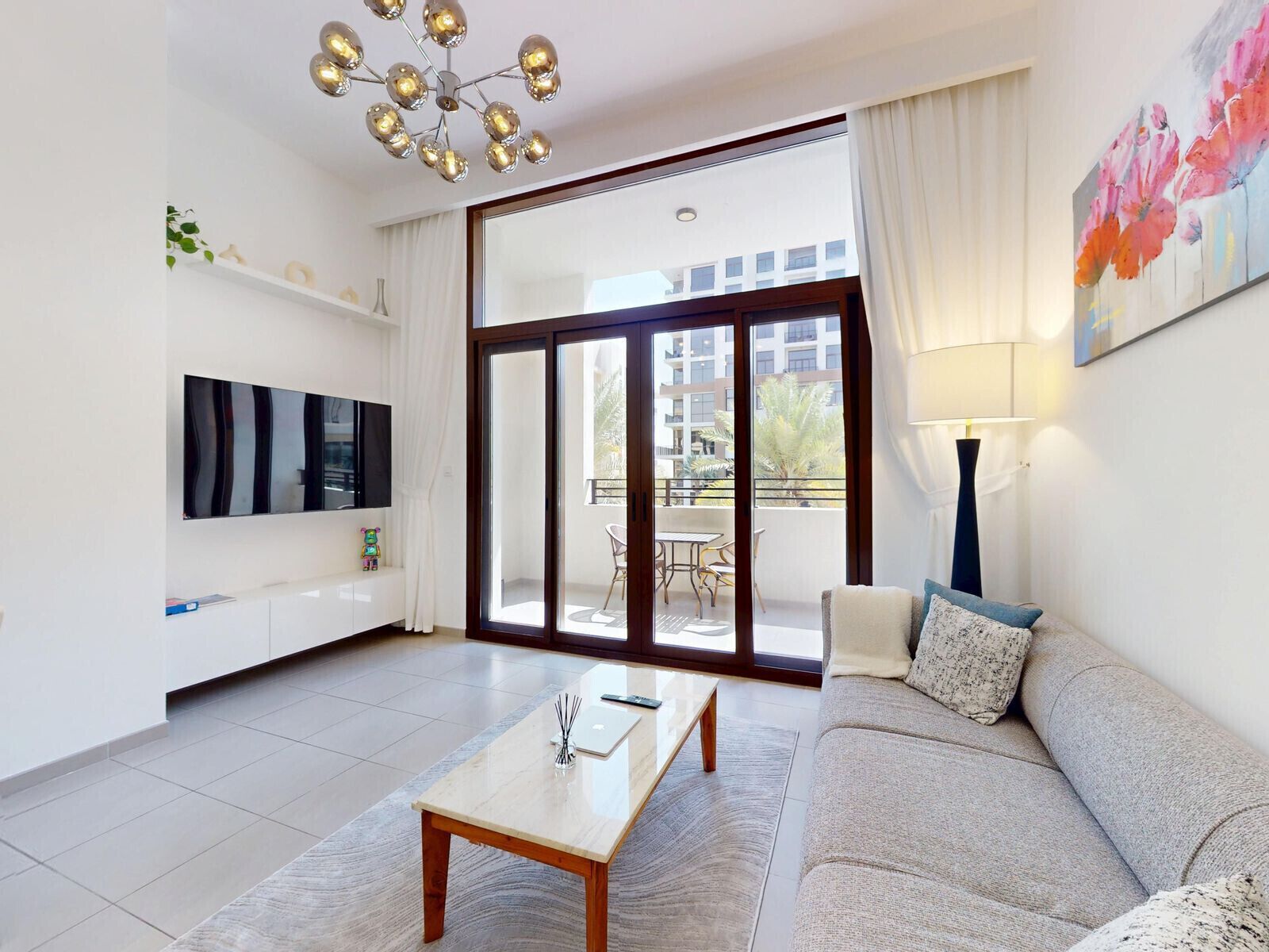 Een moderne woonkamer met een bank, een salontafel, een televisie en een balkon met uitzicht op gebouwen.