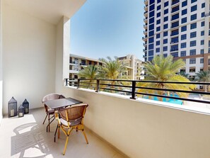 Un balcon avec une table et des chaises, donnant sur une piscine et des palmiers.