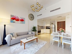 A modern living room with a sofa, coffee table, and a dining area with chairs and a table. - Modern 2BR | Fully Furnished | Great Amenities (Dubai)