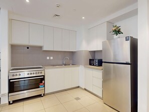 A modern kitchen with white cabinetry, a stainless steel refrigerator, a built-in oven, and a microwave. - Modern 2BR | Fully Furnished | Great Amenities (Dubai)