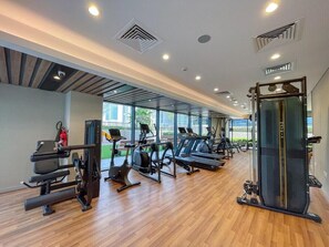 A gym with various exercise equipment, large windows, and a wooden floor. - Fully Furnished 1BR | Near Metro Station | (Dubai)