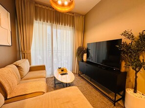 A modern living room with a sofa, a coffee table, a television, and a potted plant. - Fully Furnished 1BR | Near Metro Station | (Dubai)