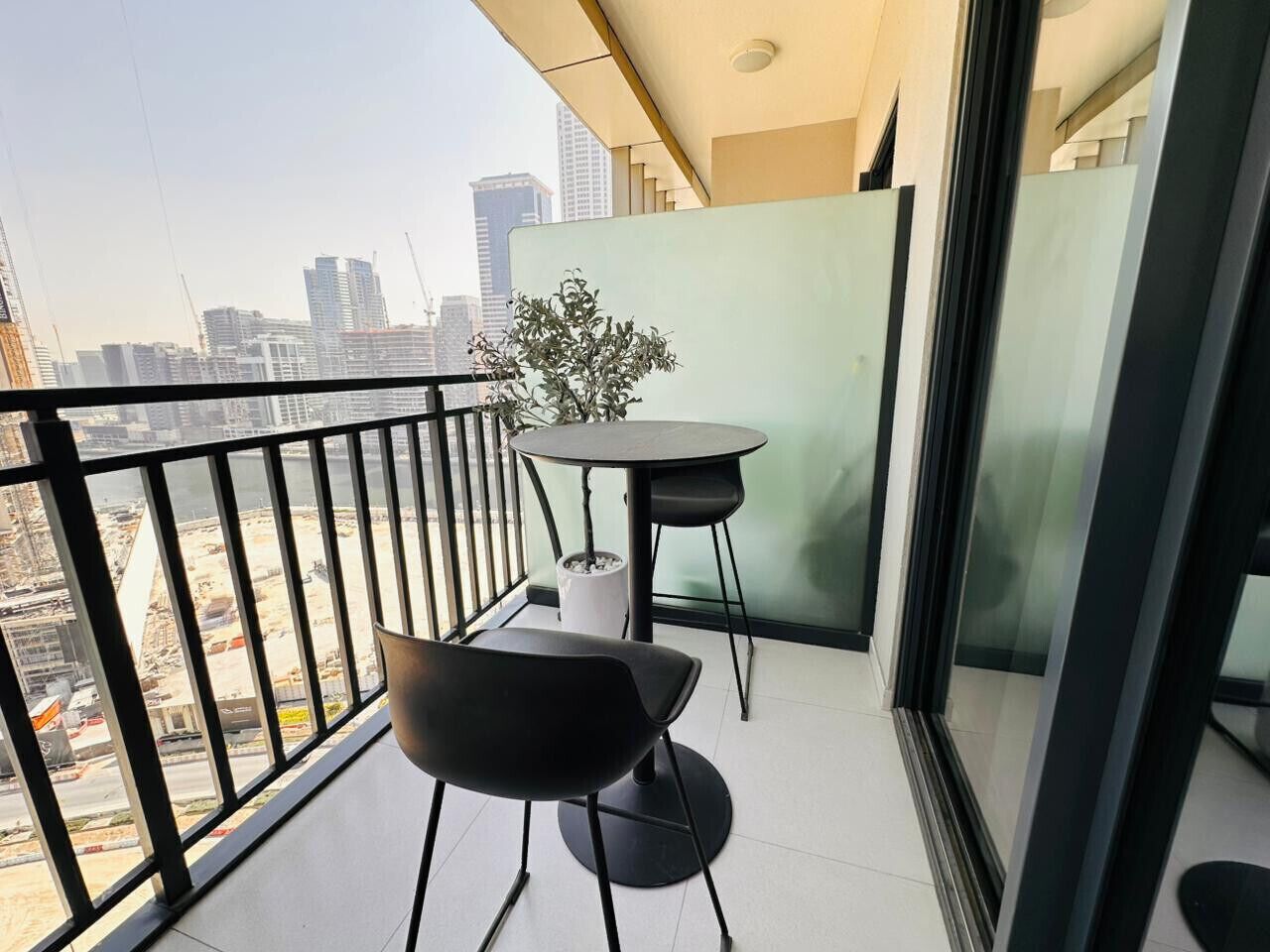 Een balkon met twee stoelen, een tafel, een bloempot en uitzicht op de stad.