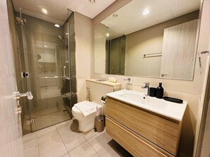 A modern bathroom with a glass-enclosed shower, a toilet, a sink with a mirror, and a vanity. - Fully Furnished 1BR | Near Metro Station | (Dubai)