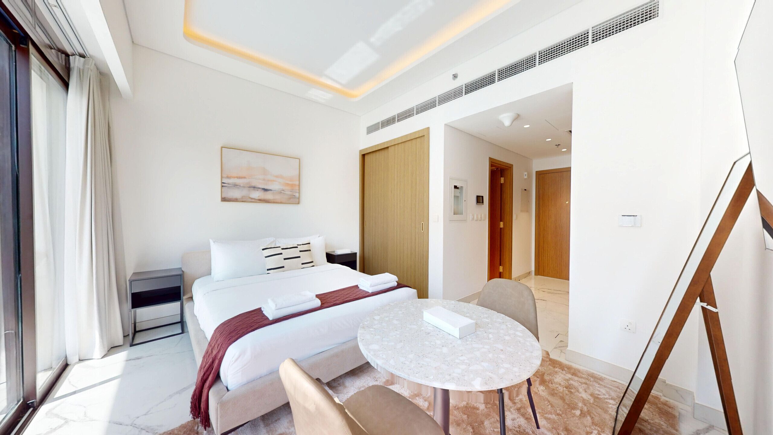 Habitación de hotel con cama, mesita de noche, silla, mesa redonda y un cuadro en la pared.