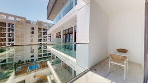 Um edifício moderno com varanda de vidro, piscina e mobiliário para exterior.
