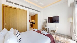A hotel room with a large bed, a desk with a chair, a TV, and a bathroom visible through an open door. - Chic Studio | Premium Amenities | Fully Furnished (Dubai)