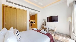 Quarto de hotel com uma cama grande, uma escrivaninha com cadeira, televisão e casa de banho visível através de uma porta aberta.