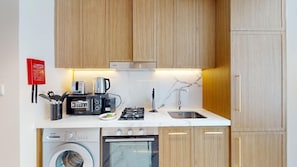 Eine kleine Küche mit Holzschränken, einer Mikrowelle, einer Kaffeemaschine, einem Spülbecken und einem eingebauten Backofen.