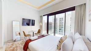 Ein Hotelzimmer mit einem großen Bett, einem Fernseher, einem Schreibtisch mit Stuhl und Blick auf die Stadt.