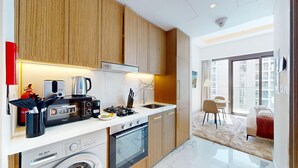 A modern kitchen with wooden cabinets, a built-in washing machine, a stove, and a coffee maker. - Chic Studio | Premium Amenities | Fully Furnished (Dubai)