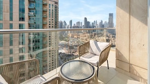 A balcony with a glass balustrade, wicker furniture, and a view of a cityscape. - Luxury Downtown Living | 2BR | High Floor (Dubai)