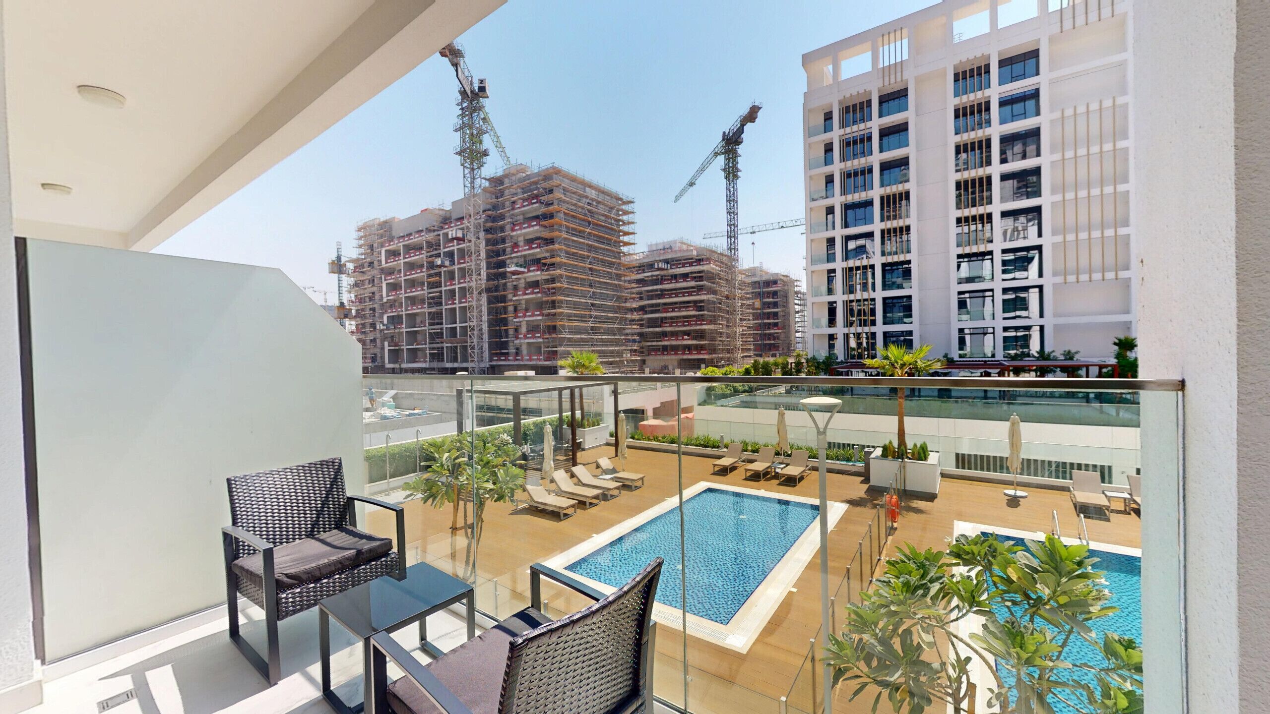 Een balkon met een zwembad, lounge stoelen en uitzicht op een bouwplaats.
