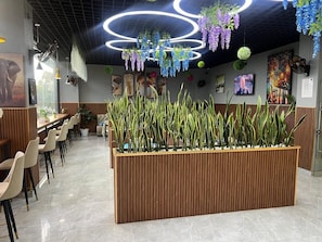 A modern restaurant interior with a long wooden counter, multiple seating areas, and decorative hanging plants.