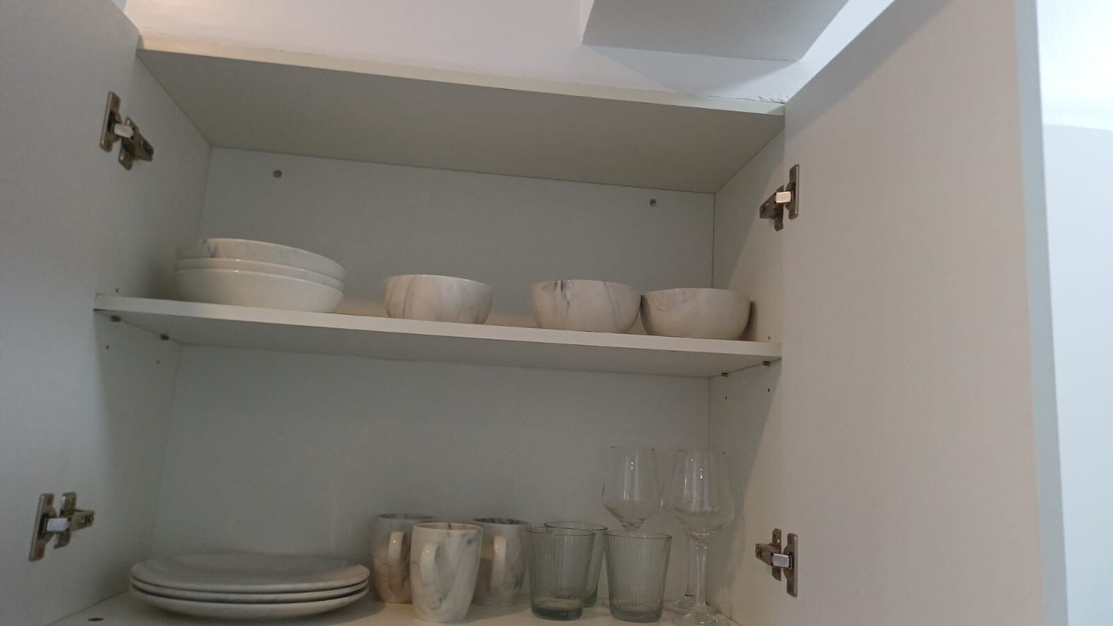 Un armario de cocina con estantes que sostienen cuencos, platos y vasos.
