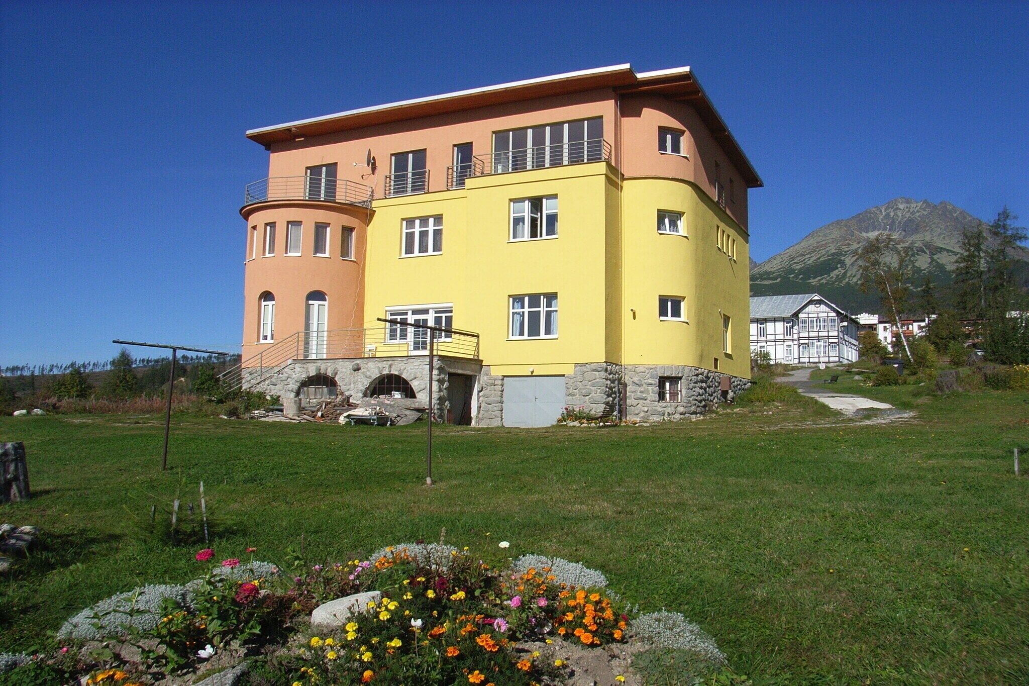 A multi-story building with a stone base and a yellow upper section, surrounded by a grassy area with flowers.
