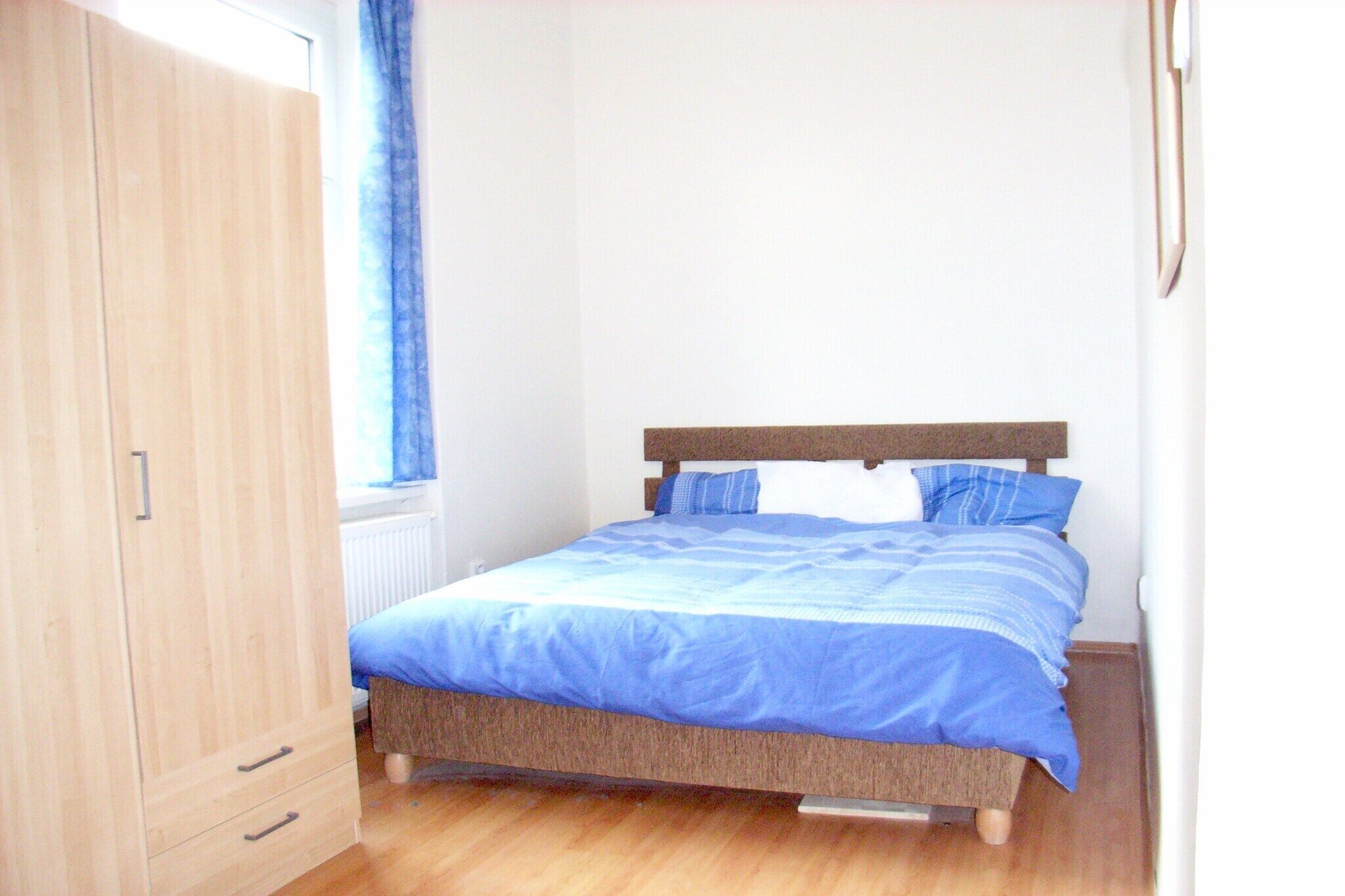 A bedroom with a bed, wooden wardrobe, and a window with curtains.
