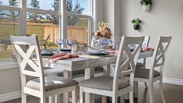 Un coin repas avec une table dressée pour quatre personnes, entourée de chaises blanches dotées d’assises rembourrées.