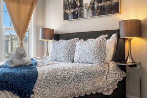 Ein ordentlich bezogenes Bett mit Blumenmuster, zwei Nachttische mit Lampen, ein Handtuch und ein Bild an der Wand.