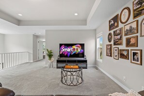 Ein Wohnzimmer mit Flachbildfernseher, einem Esstisch und einer Treppe, die zu einer weiteren Ebene führt.