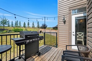 En terrasse med grill, udendørs møbler og udsigt til en græsplæne med træer.