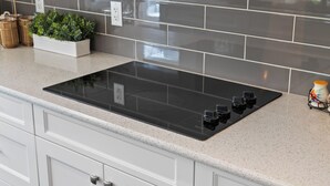 Une cuisine dotée d’une plaque de cuisson à induction noire, de meubles blancs et d’un dosseret carrelé gris.
