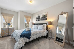 A bedroom with a large bed, a bedside table, a mirror, and a window with curtains. - *Nolancrest Luxury Retreat| Spacious Home with AC* (Calgary)