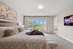 Ein Schlafzimmer mit einem großen Bett, einem Fenster mit Blick auf Bäume und ein Gebäude sowie einem Gemälde an der Wand.