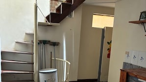 A staircase with metal railings, a white trash bin with bird illustrations, a patterned floor, and a wooden stool.