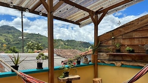 A hammock on a balcony with potted plants and a view of a mountainous landscape.