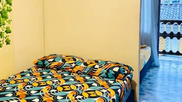 Ein Zimmer mit einem Bett, einer Topfpflanze und Blick auf ein Ziegeldach durch eine offene Tür.