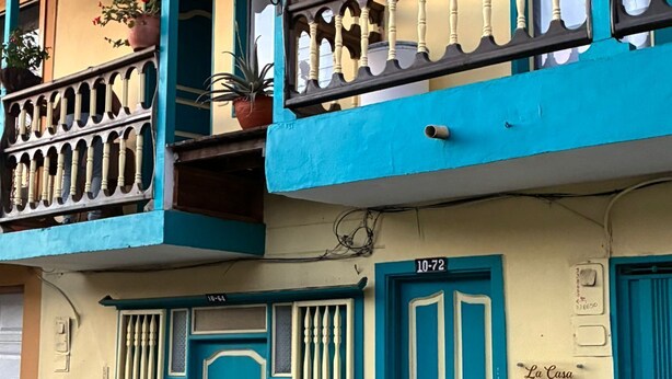 Un bâtiment à la façade bleue et crème, orné de balcons où sont disposées des plantes en pot, et sur lequel on peut lire l’inscription « La Casa Del Pueblo » ainsi que le numéro « 10-72 ».