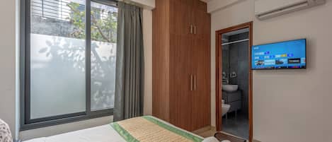 Habitación de hotel con una cama grande, un armario, un televisor y un baño visible a través de una puerta abierta.