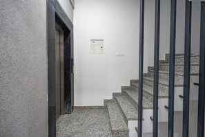 A staircase with granite steps and black railings, leading to a door with a small, white intercom panel above it. - Divine India Service Apartment E-69 Spacious 3 Bedroom with AC & Balcony (New Delhi)