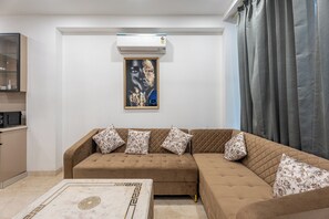 A living room with a brown sofa, a marble coffee table, and a wall-mounted air conditioner. - Divine India Service Apartment E-69 Spacious 3 Bedroom with AC & Balcony (New Delhi)