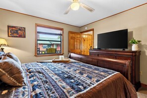 A bedroom with a bed, a television, a dresser, a window with blinds, and a ceiling fan. - Cozy Cabin + Hot Tub + Decks | Arcade + Mountain Views Near Park | Dancing Bear (Pigeon Forge)
