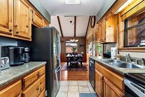 Una cocina con armarios de madera, un refrigerador, una cafetera y un comedor con mesa y sillas.