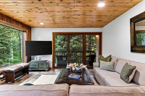 Ein gemütliches Wohnzimmer mit Holzboden, einem großen Fenster, einem Flachbildfernseher, einer Couch und einem Couchtisch.