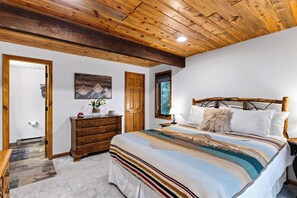 A bedroom with a wooden ceiling, a bed with a striped blanket, a dresser, and a painting on the wall. - Mtn Views + Balcony | Trailheads + Free Ski Bus | Falls & Firs (Vail)