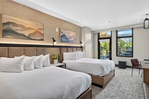 A hotel room with two beds, a desk, a chair, and large windows offering a view of the outdoors. - Steps to Gondola • Shared Pool + Mountain Views • Resort Access | Gondola & Gold (Avon)
