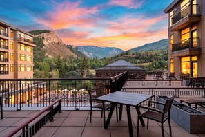 A hotel balcony with outdoor seating, a view of mountains, and a hotel building. - Steps to Gondola • Shared Pool + Mountain Views • Resort Access | Gondola & Gold (Avon)
