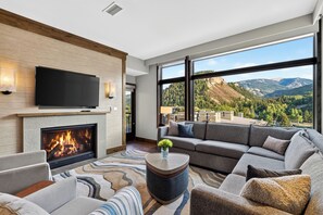 A modern living room with a fireplace, a large flat-screen TV, and a sofa set. - Ski Valet + Resort Pool + Hot Tubs | Valley Views | Riverfront Perch (Avon)