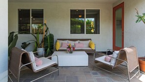 En overdækket patio med sofa, to stole, et sofabord og potteplanter.