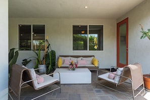 Ein überdachter Patio-Bereich mit einer Couch, zwei Stühlen, einem Couchtisch und Topfpflanzen.