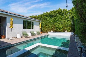 Ein Pool mit Fliesen, grüne Liegestühle und ein weißes Gebäude mit einem Flachdach.