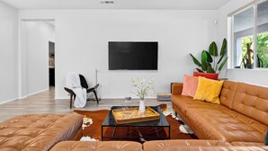 En moderne stue med en lædersofa, et sofabord og et fladskærms-tv monteret på væggen.